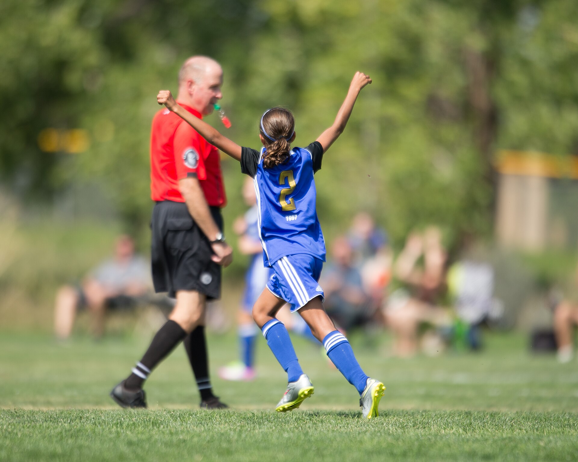A young player throws both arms up in celebration as the referee looks on