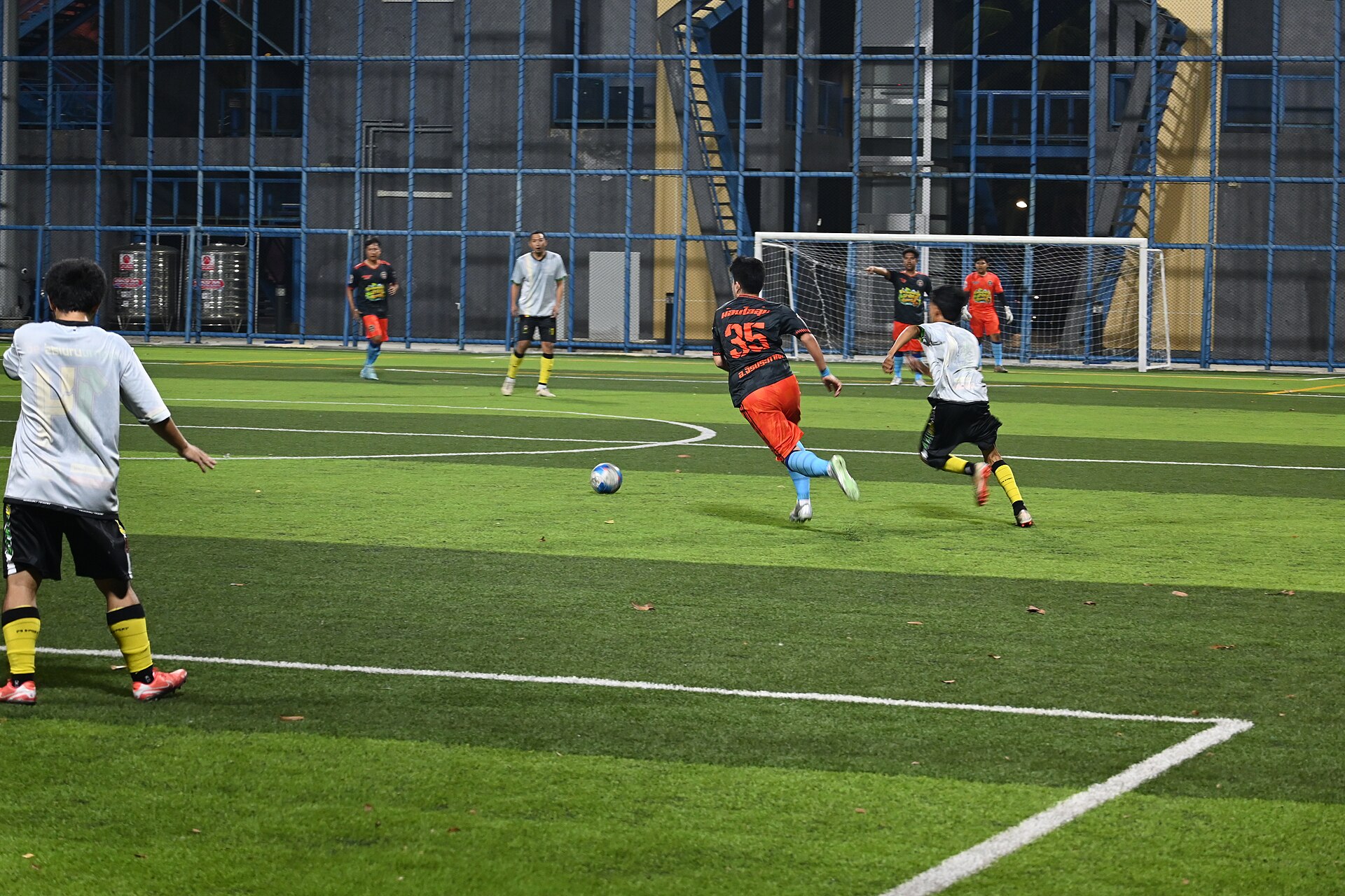 A night match under floodlights — a player sprints toward goal as defenders close in