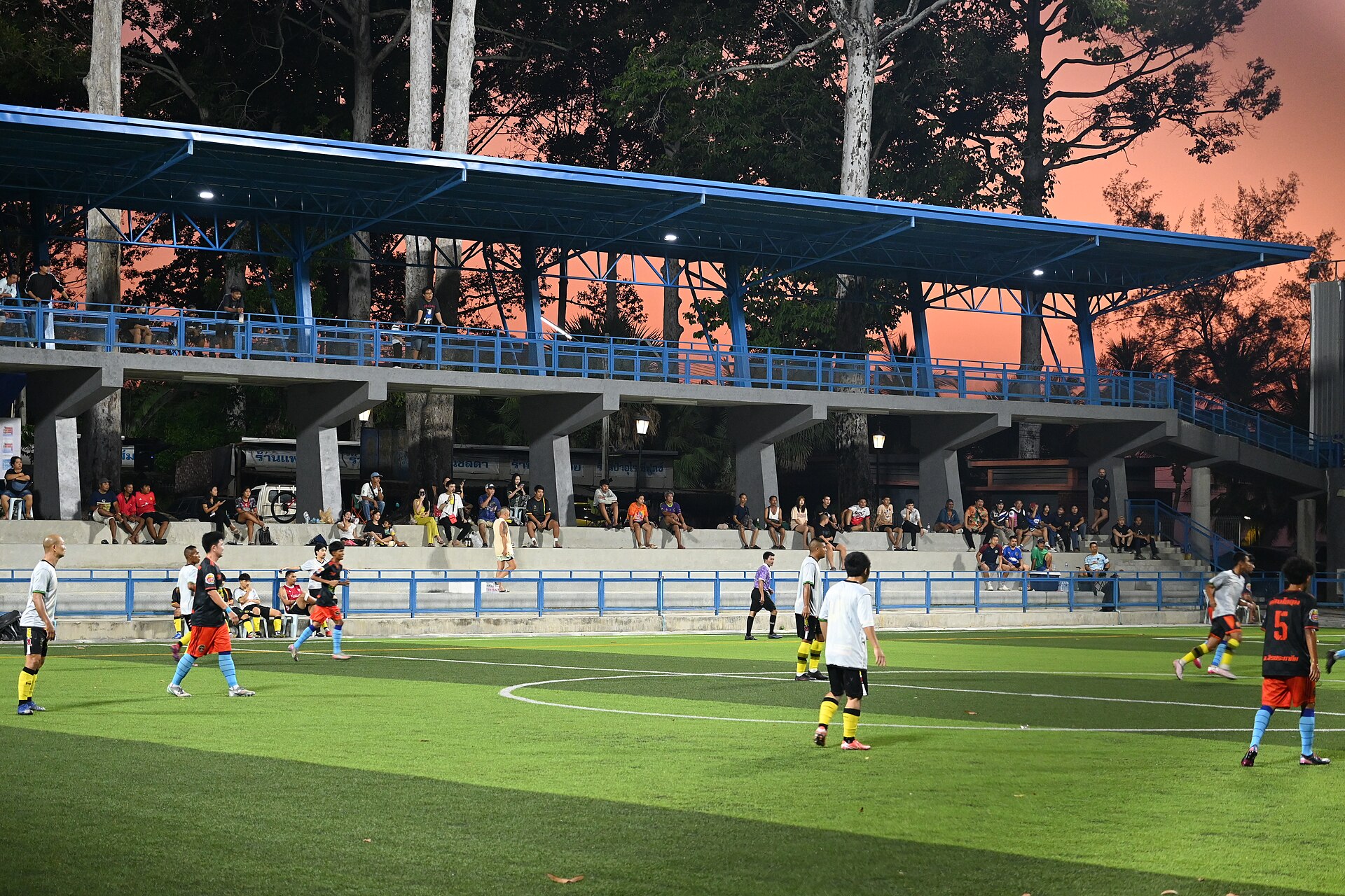A tournament evening match under floodlights as spectators fill the stands at sunset